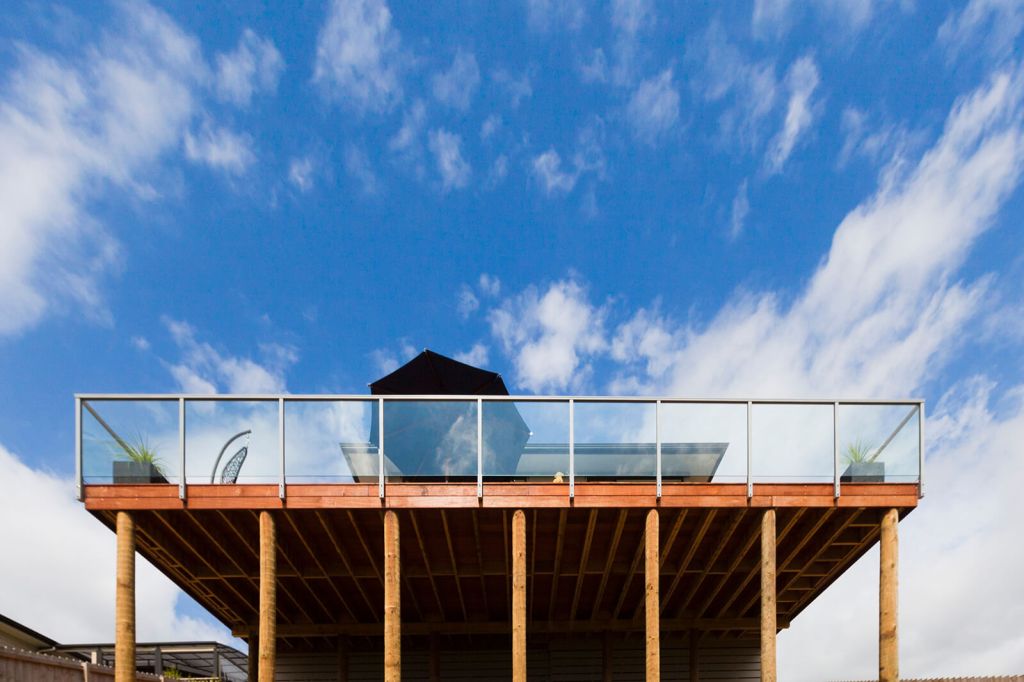 Frameless glass balustrade installed on a wooden deck, showcasing a modern outdoor space with a clear view and wooden pillars beneath.