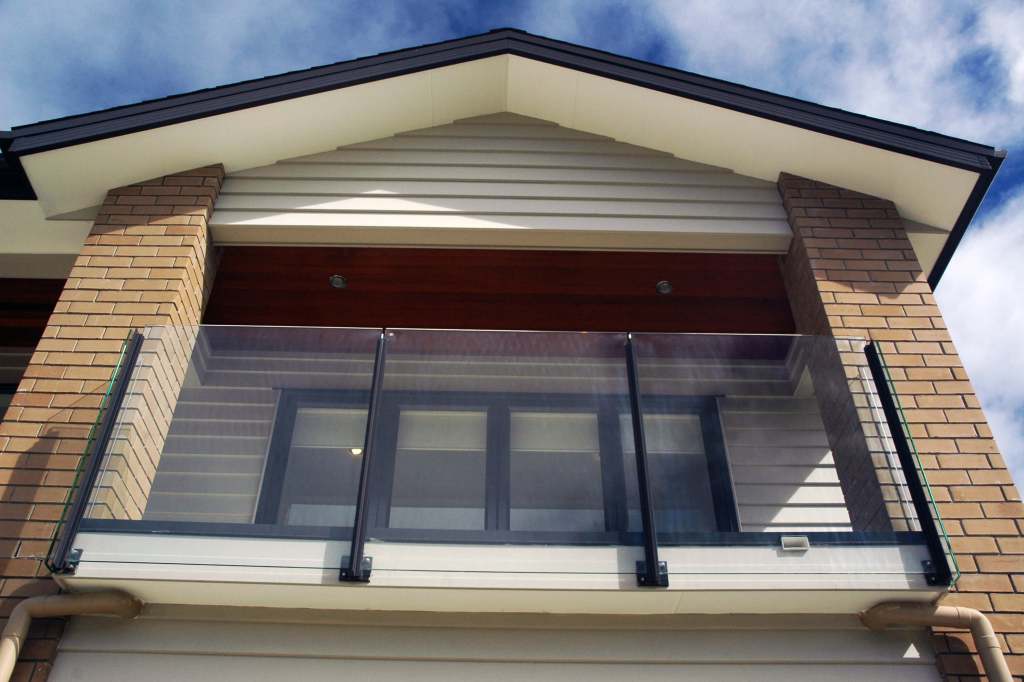 A modern frameless glass balustrade installed on a residential balcony, featuring stainless steel fixings and overlooking a clear sky.
