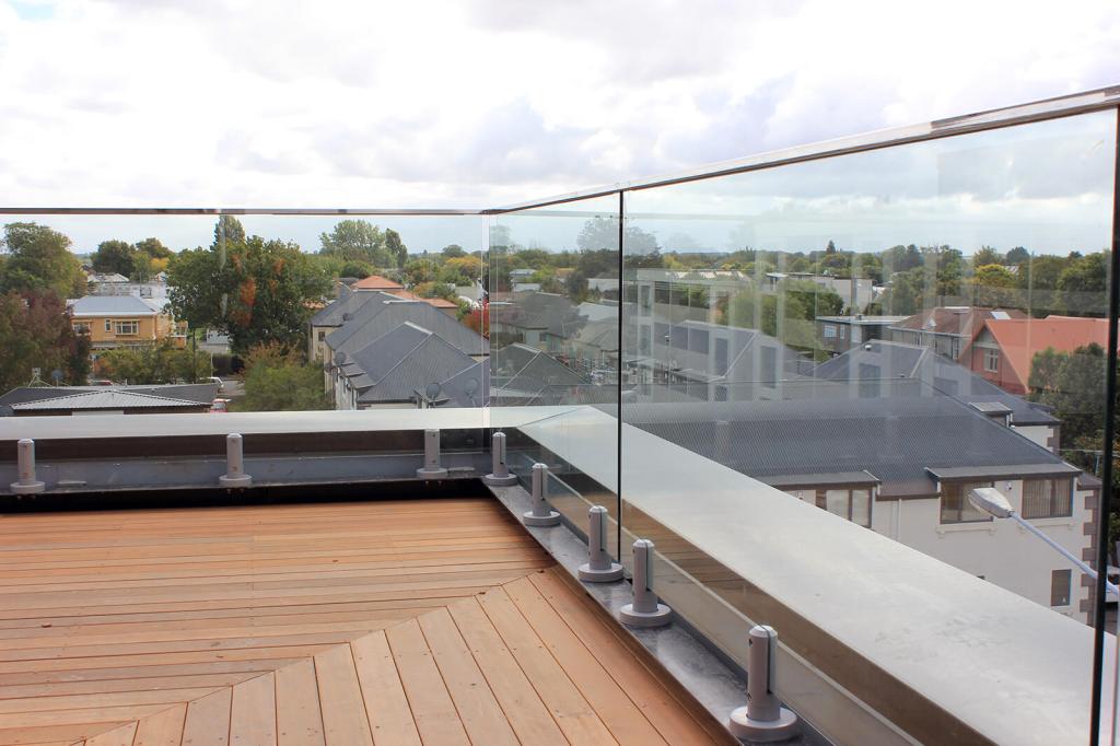 A frameless glass balustrade installed on a wooden terrace, providing an unobstructed view of the surrounding neighborhood and trees.
