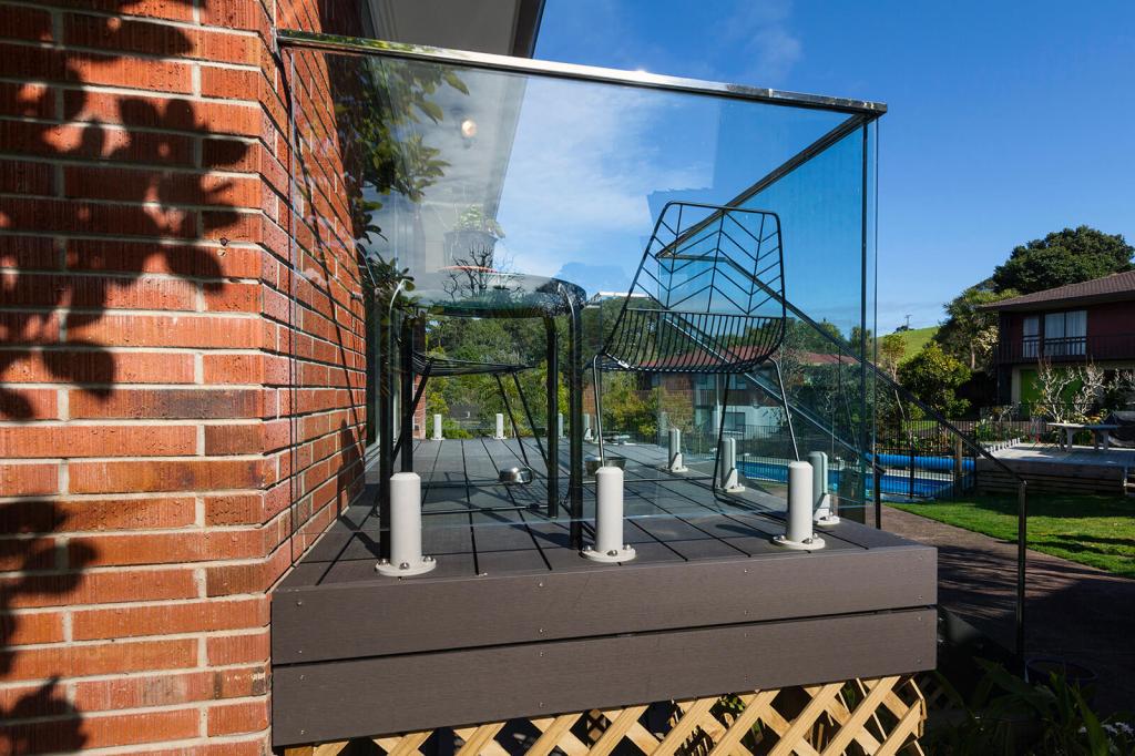 Frameless glass balustrade installed on a wooden deck with a view of a garden and houses in the background.