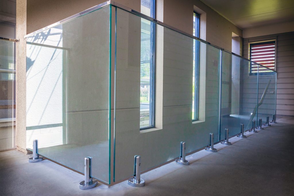 Frameless glass balustrade installation featuring stainless steel clamps, providing a sleek and modern aesthetic in a well-lit interior space.