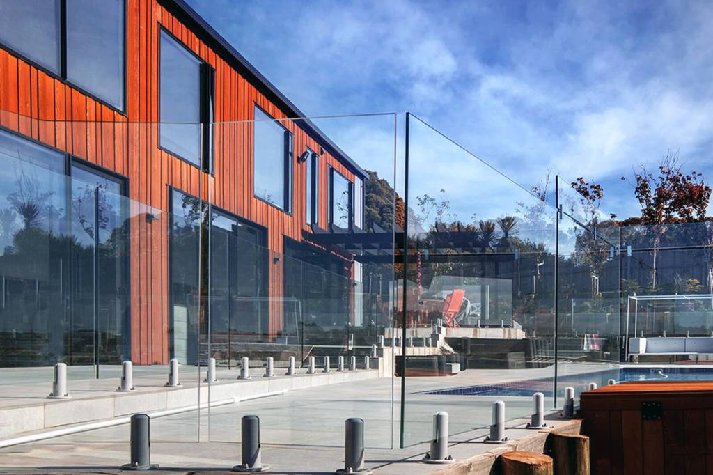 Exterior view of a modern building featuring frameless glass balustrades around a patio area, showcasing a blend of natural materials and contemporary design.