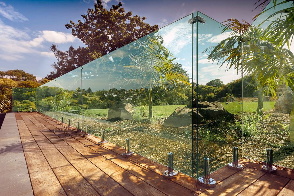 Frameless glass balustrade installed on a wooden deck, offering a clear view of the surrounding landscape with lush greenery and rocks.