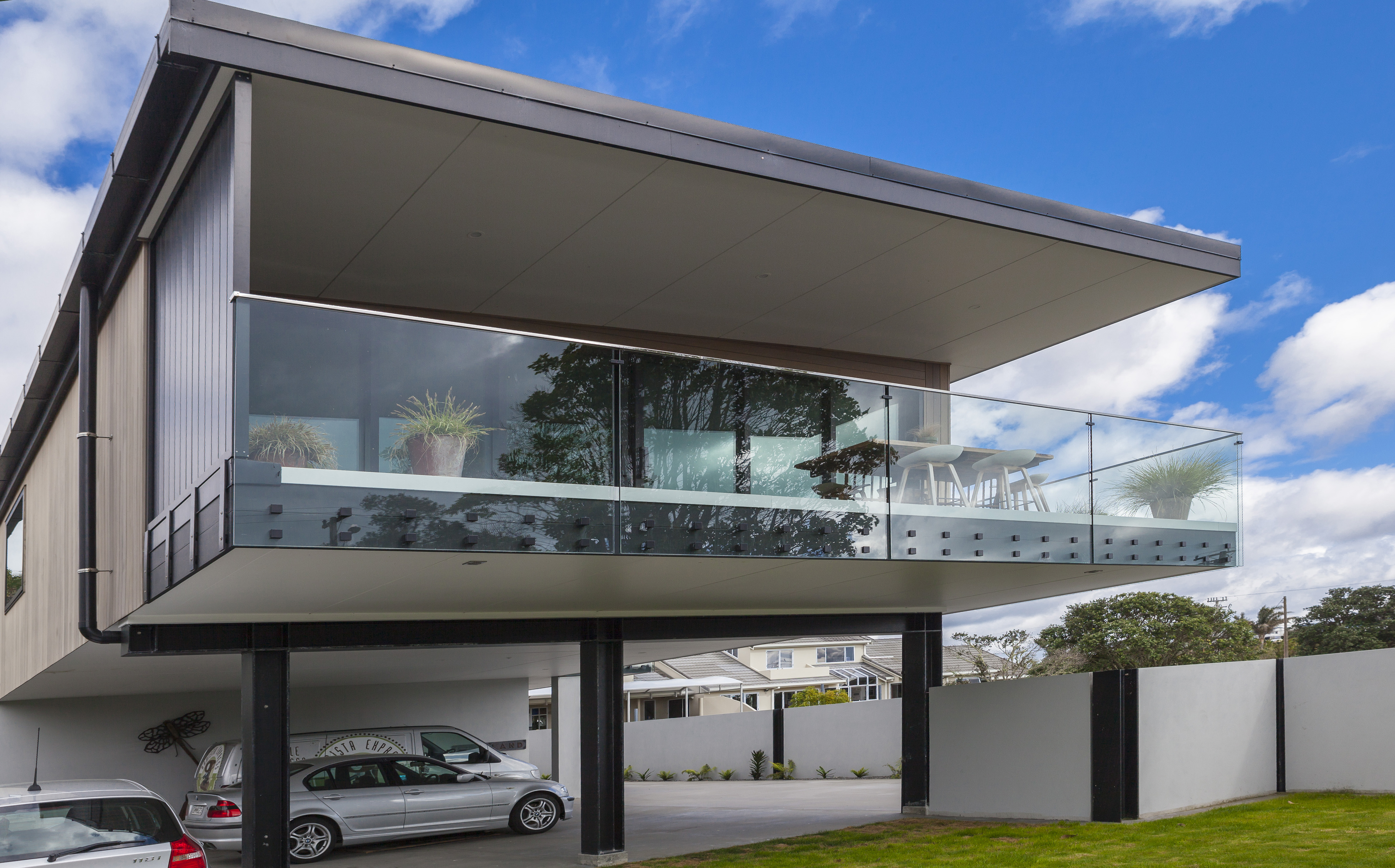 Modern house featuring a frameless glass balustrade on a balcony, showcasing a contemporary architectural design against a bright sky.